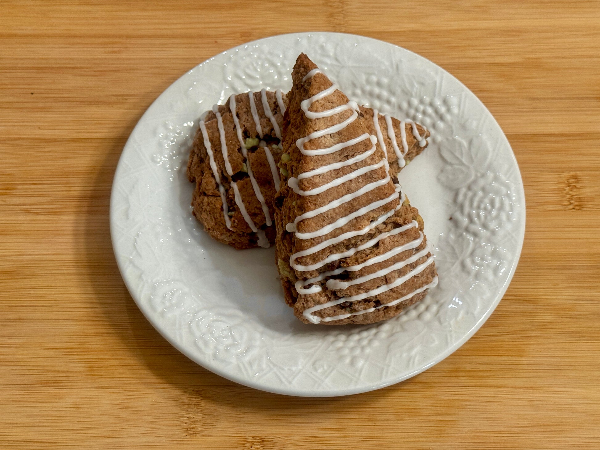 Two chocolate mint scones with white drizzle on a white plate on a wooden surface