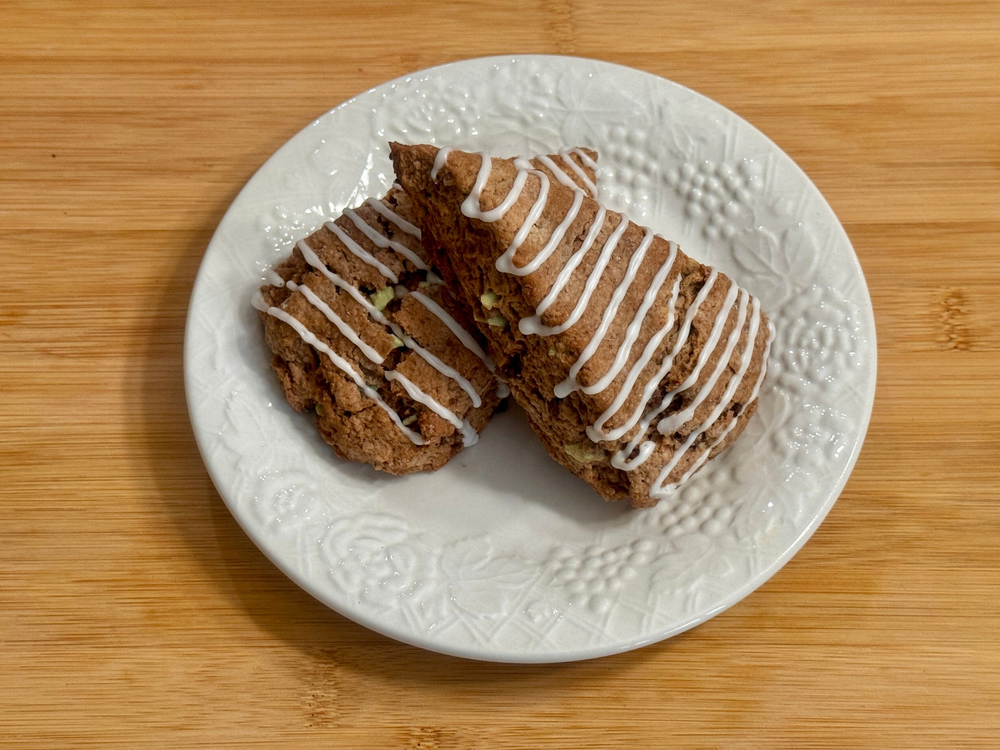 Two peppermint mocha scones with mint icing on a white plate on a wooden surface
