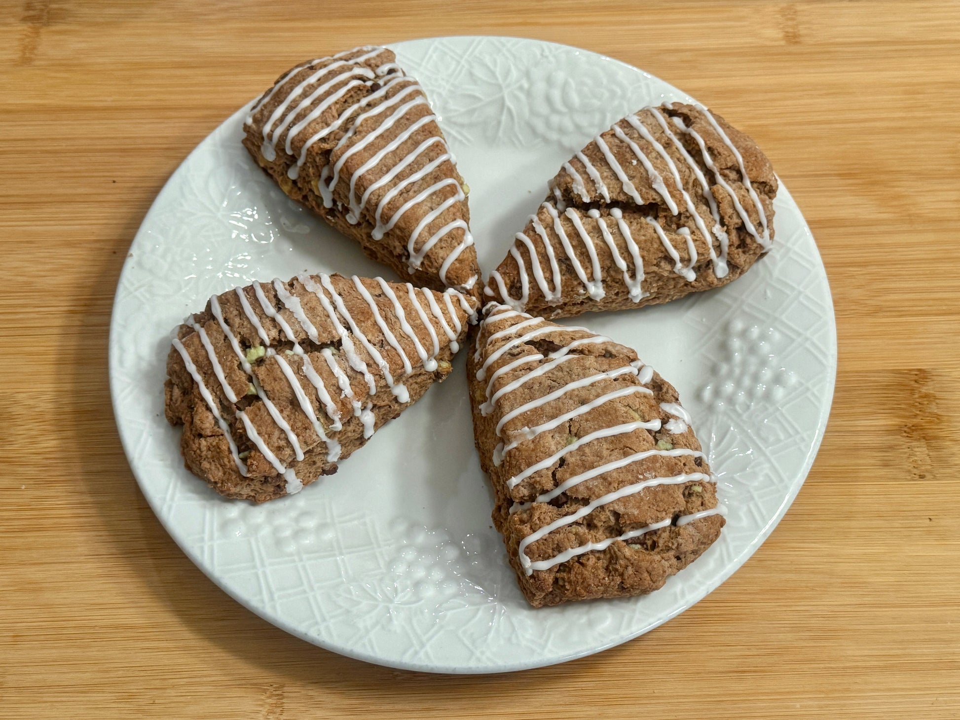 Four mint chocolate scones with white drizzle on a white plate on a wooden surface