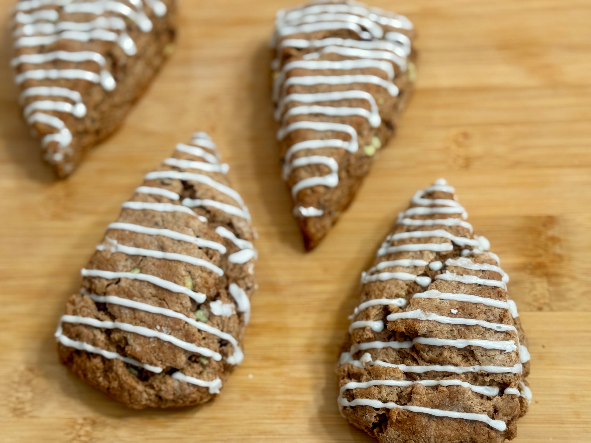 four mint chocolate scones with white drizzle on a wooden surface