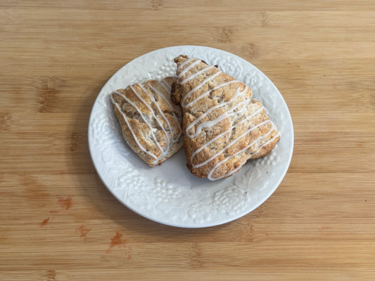 Two strawberry scones with icing on a white plate on a wooden surface