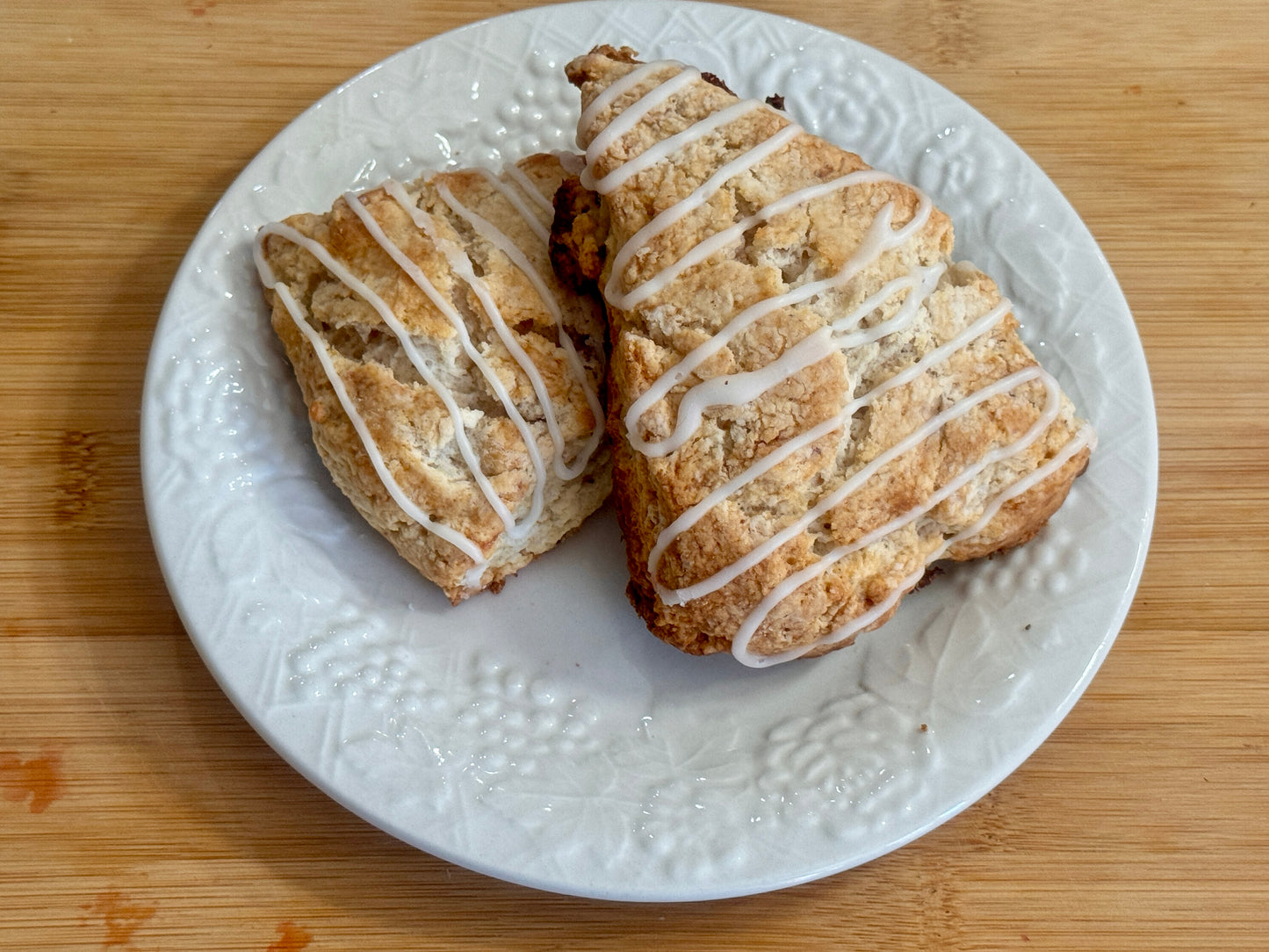 Two strawberry scones with icing on a white plate on a wooden surface