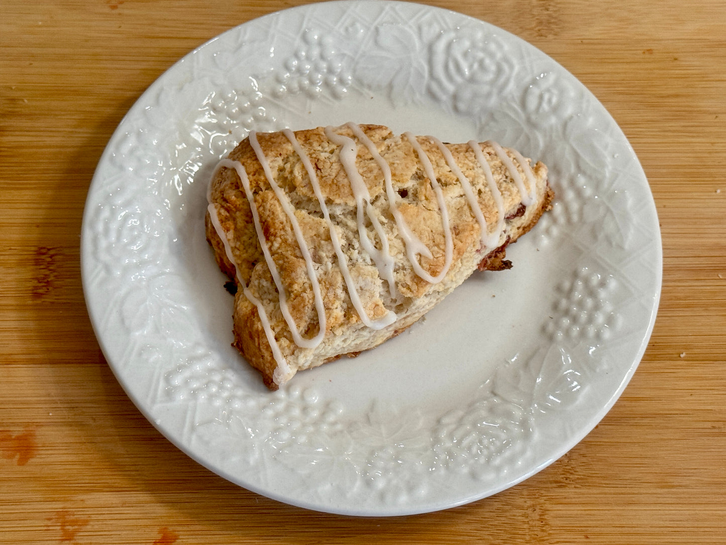 Strawberry Scone with icing on a white textured plate on a wooden surface