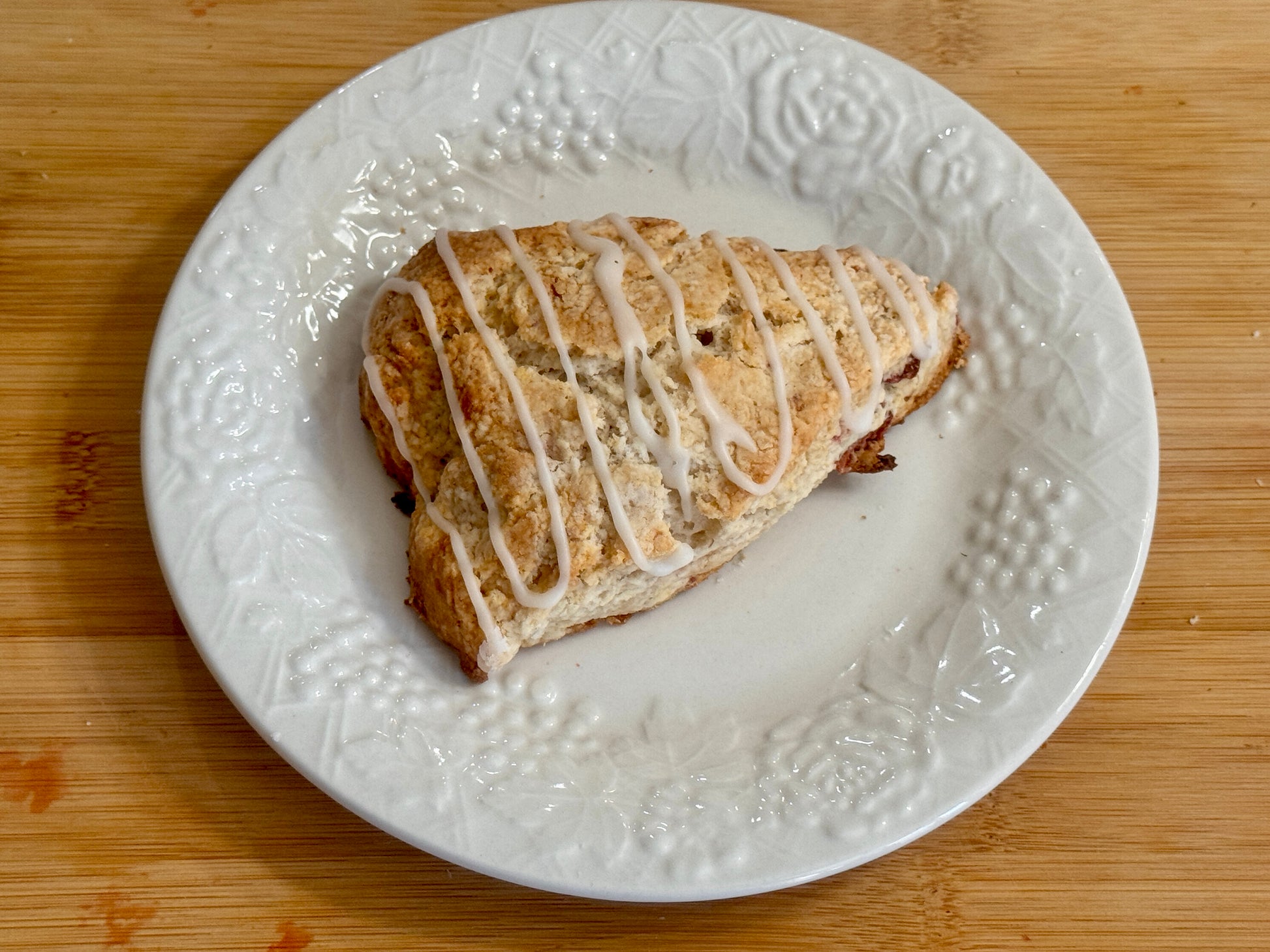 Strawberry Scone with icing on a white textured plate on a wooden surface