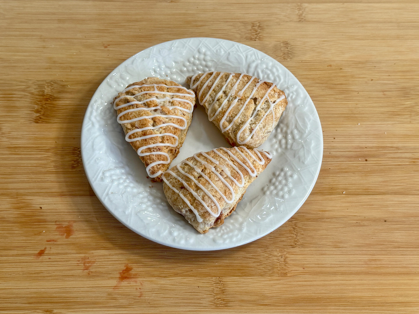 Three strawberry mini scones with icing on a white plate on a wooden surface