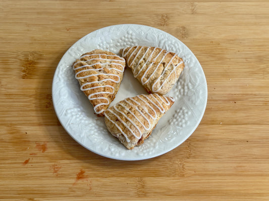 Three strawberry mini scones with icing on a white plate on a wooden surface