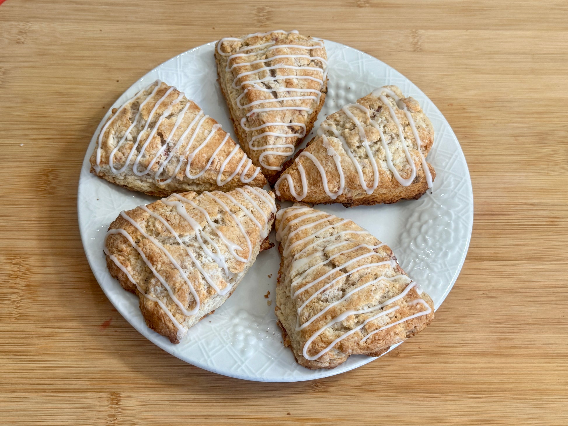 Five strawberry scones with icing on a white plate on a wooden surface
