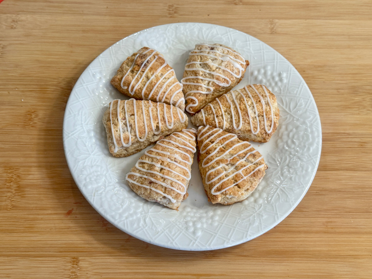White plate with six iced strawberry scones on a wooden surface