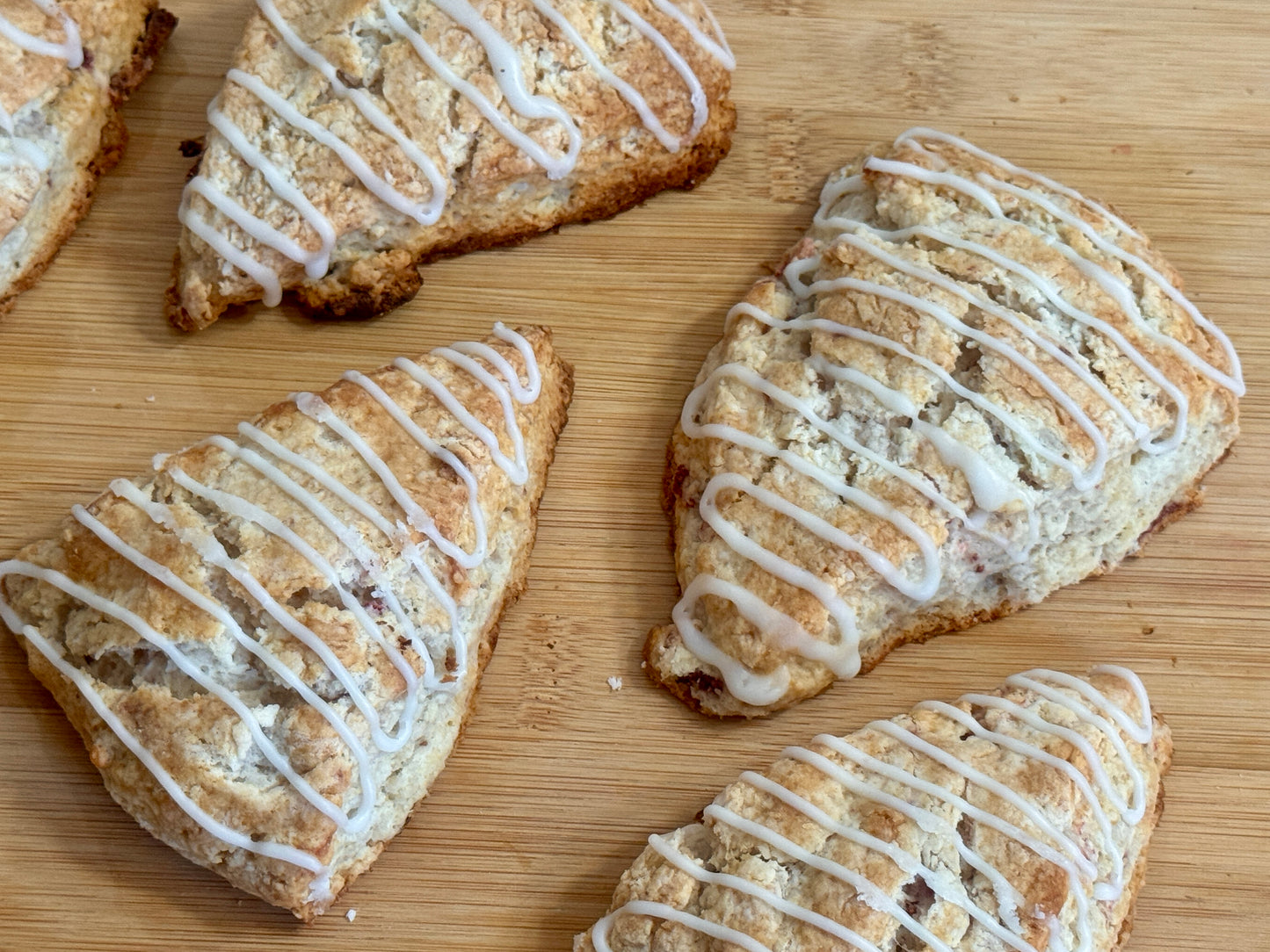 Baked strawberry scones with white icing on a wooden surface