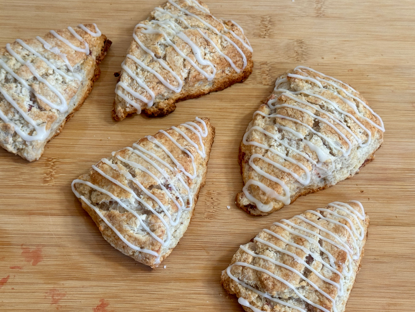 Five strawberry scones with white icing on a wooden surface