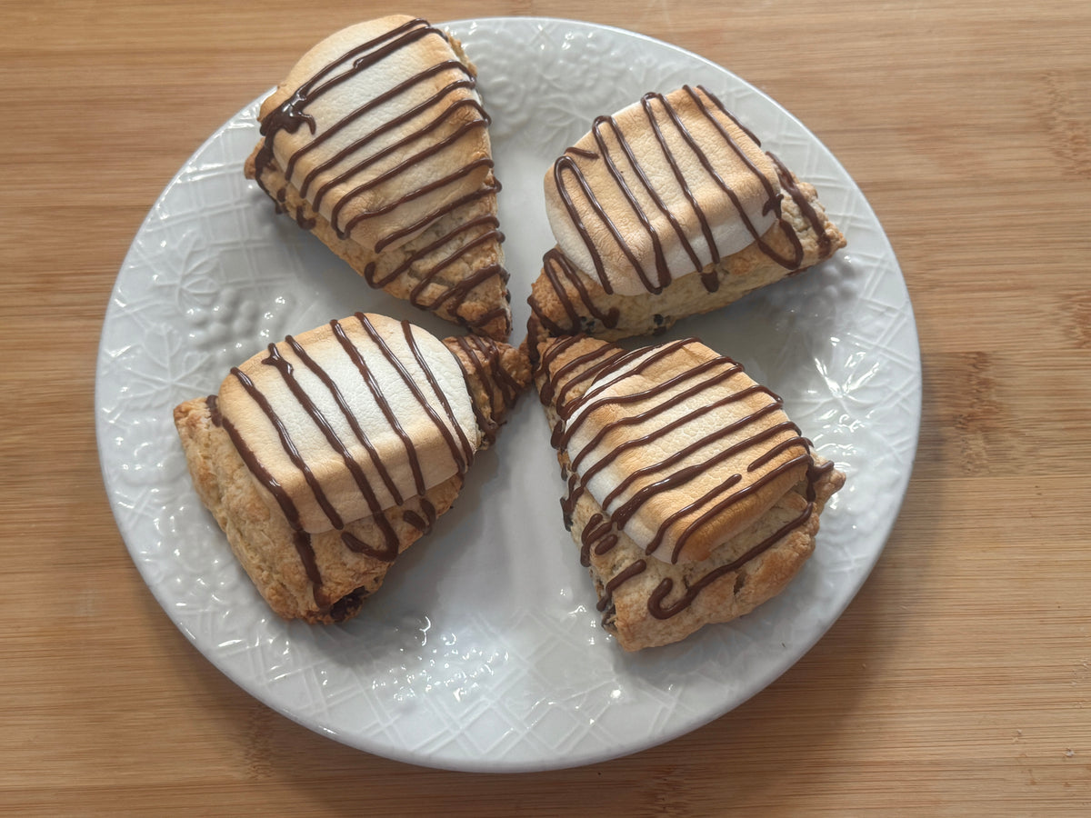 Four regular sized s'mores scones arranged on a white plate over a light wood surface.